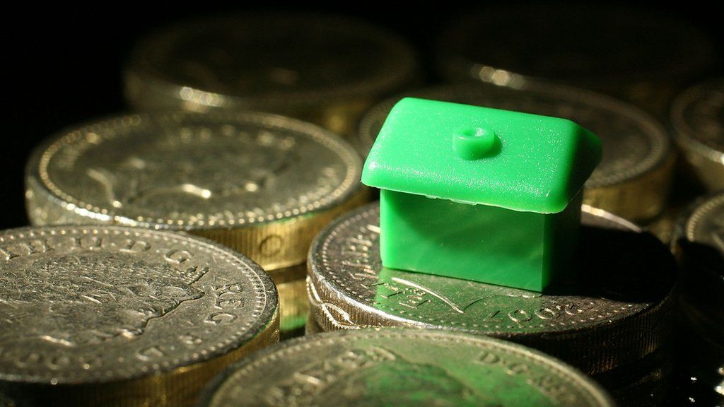 A Monopoly house sits among pound coins