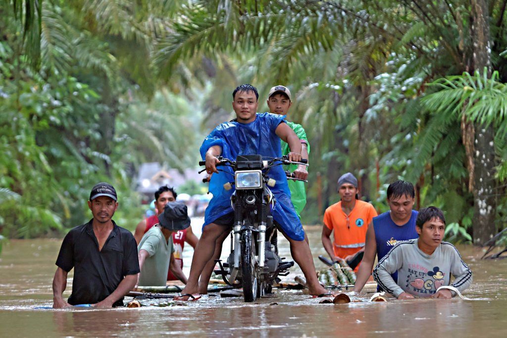 Residents push a makeshift raft loaded with a motorcycle through floodwaters