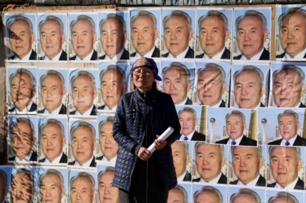 Woman standing outside her home plastered with images of the Kazakh president