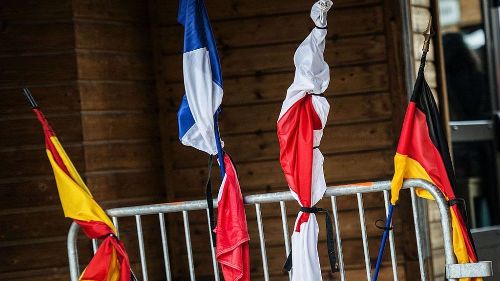 A Spanish, French, Japanese and German flag tied with black ribbon are attached to a gate in memory of the victims of the Germanwings Airbus A320 crash, in the village of Le Vernet, south-eastern France, on March 28, 2015, near the site where plane crashed in the French Alps.