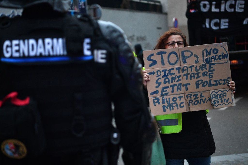 Manifestante sosteniendo un cartel anti-vacuna frente a gendarmes.
