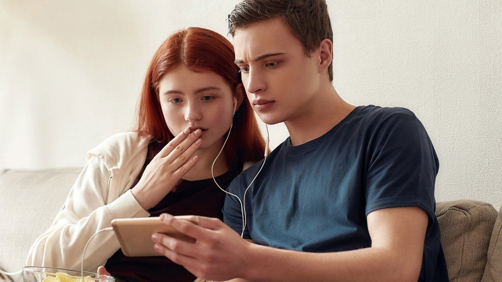 Stock image of teenagers looking worried watching a phone video
