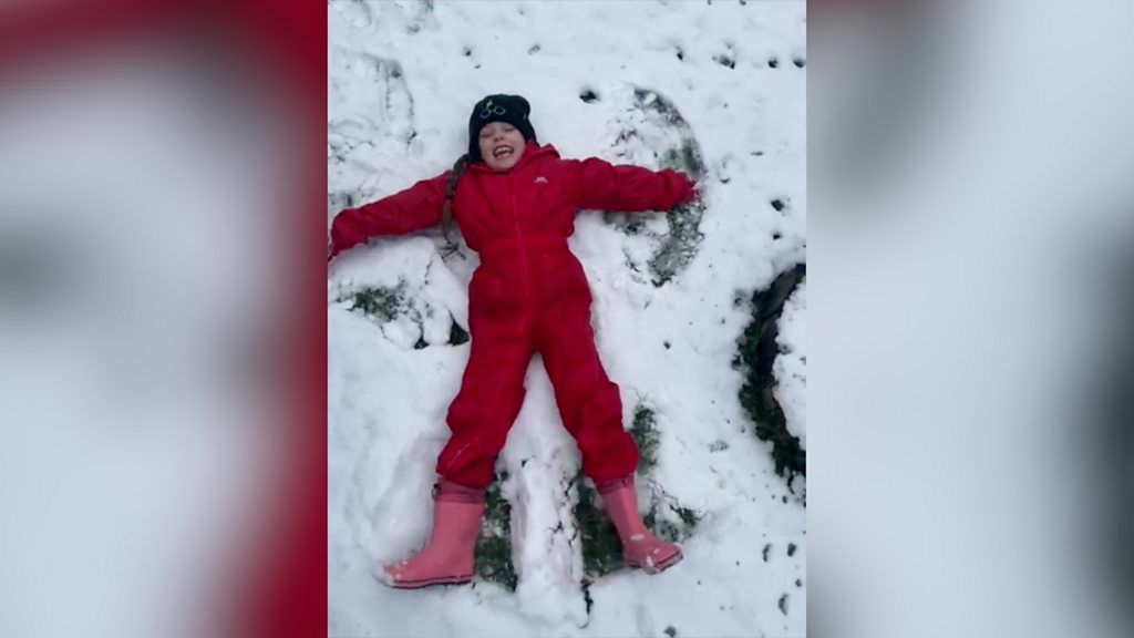 little girl lying on her back in the snow making a snow angel