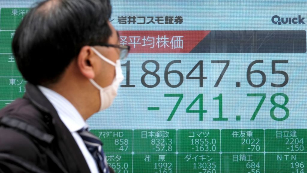 A man wearing a fast mask walks past a quotation board displaying share prices of the Tokyo Stock Exchange in Tokyo on March 30, 2020