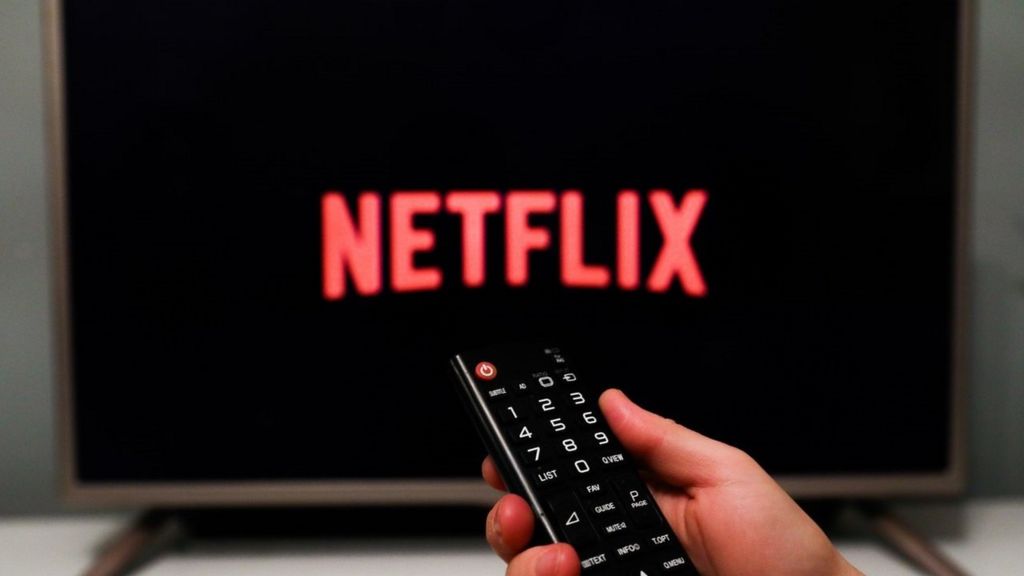 Netflix logo on a TV with hand holding remote