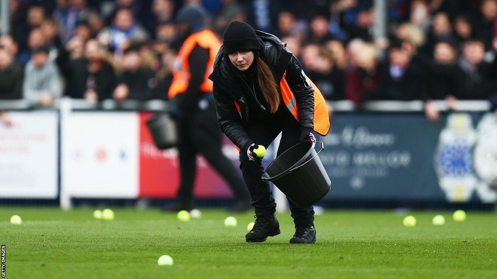Steward picking up tennis balls off the pitch following Reading fans' protest during FA Cup[ second round tie v Eastleigh