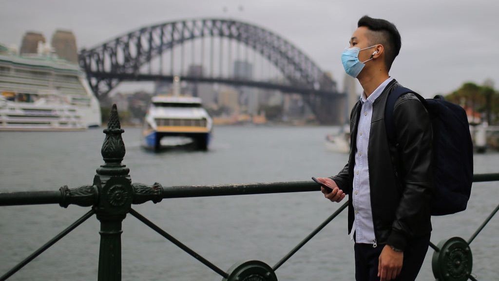 A man wears a face mask in front of the Sydney Harbour Bridge in Sydney, Australia.