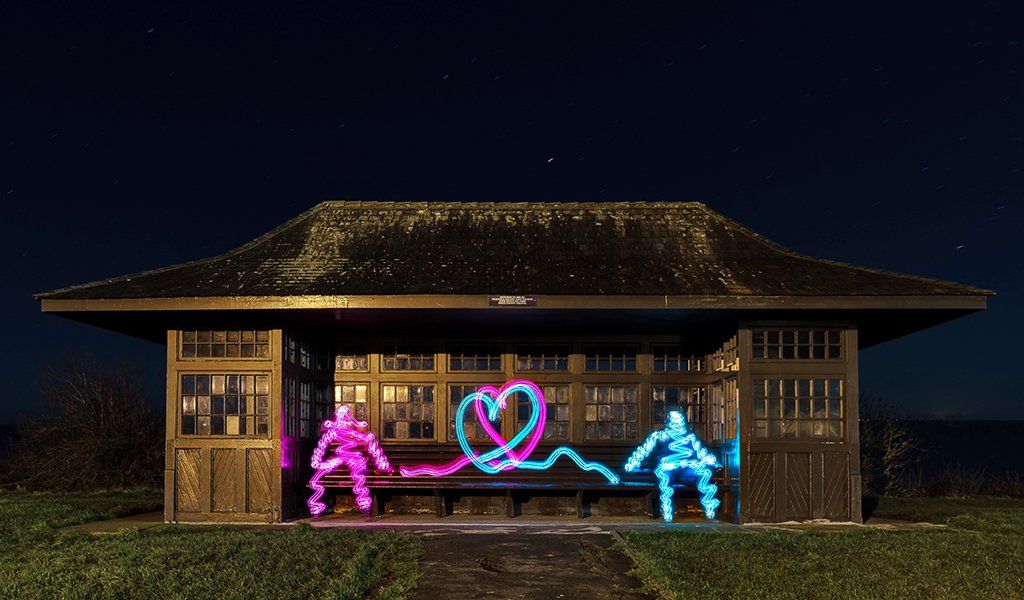 Figures painted out of light sitting in a shelter on Frinton beach