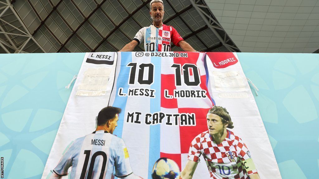A fan poses with a half-and-half Argentina-Croatia jersey, along with a banner bearing images of Lionel Messi of Argentina and Luka Modric of Croatia, during the last-16 World Cup tie between Japan and Croatia