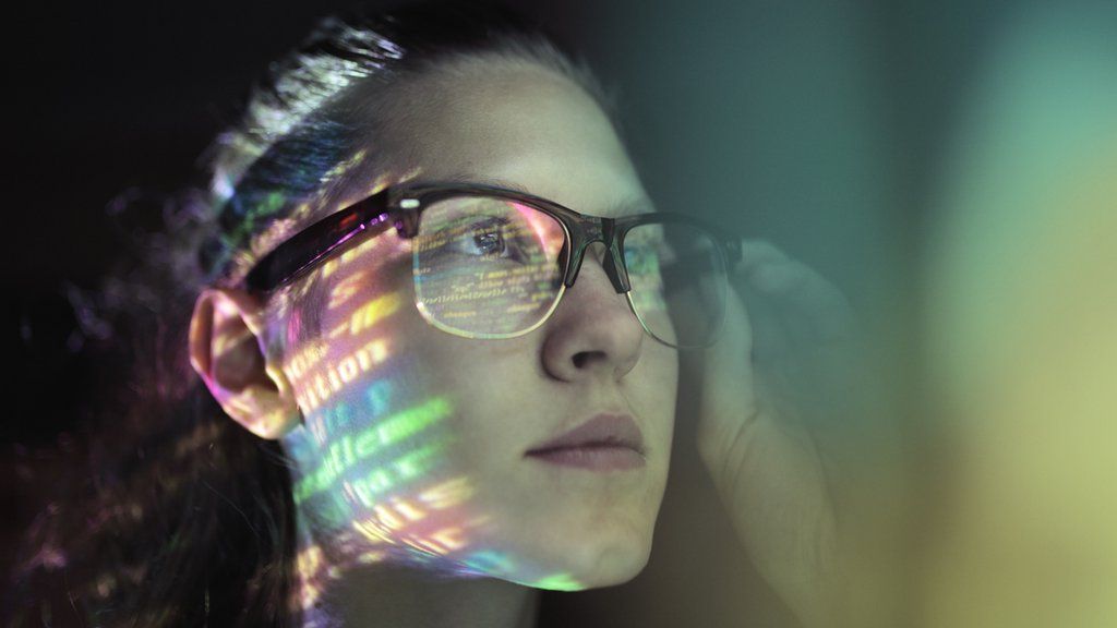 A woman's face is lit up with strings of code