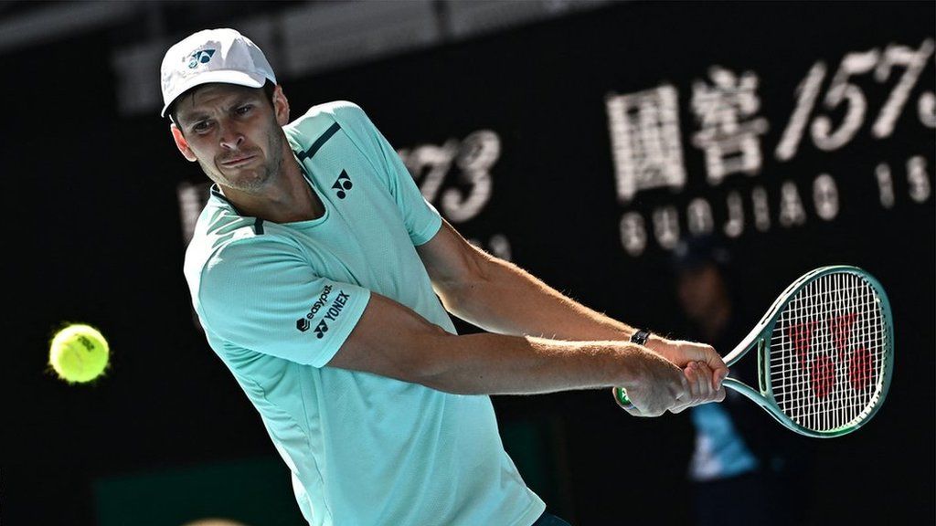 Hubert Hurkacz hits a backhand shot wearing a white shirt and white cap