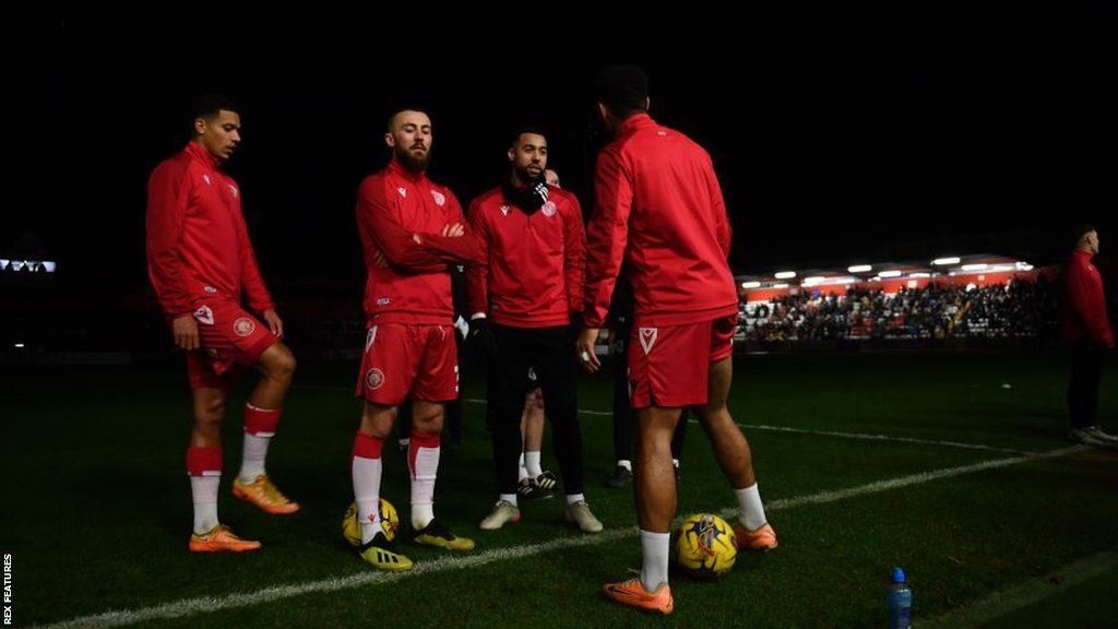 Players stand around waiting for the floodlights to be fixed