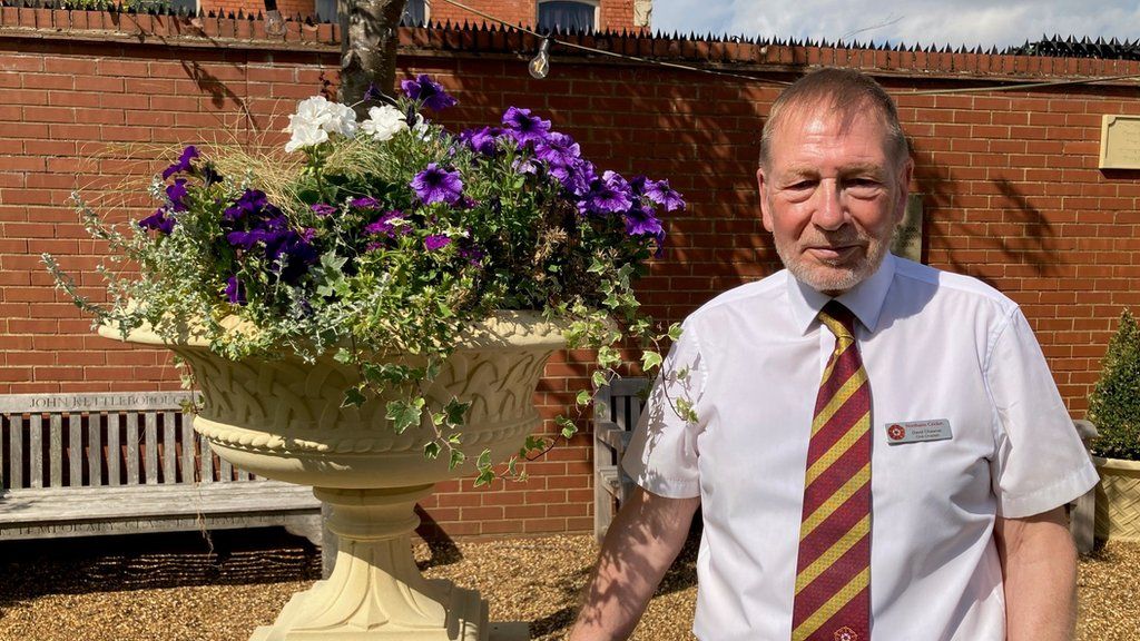 Man in cricket club tie stands next to a stone plinth