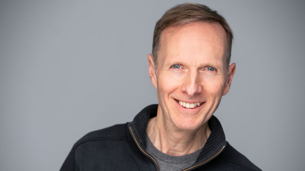 A professional picture of Councillor Mark Topping smiling and looking into the camera against a plain grey background.  