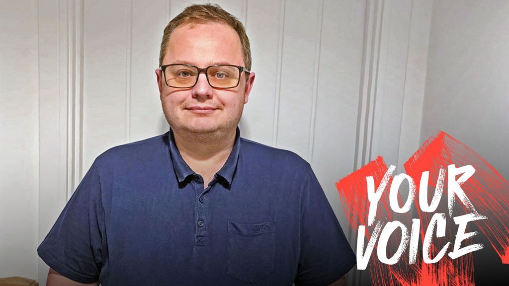 Sam Gillson, wearing glasses and a blue polo shirt, with Your Voice branding on the right hand side of the picture