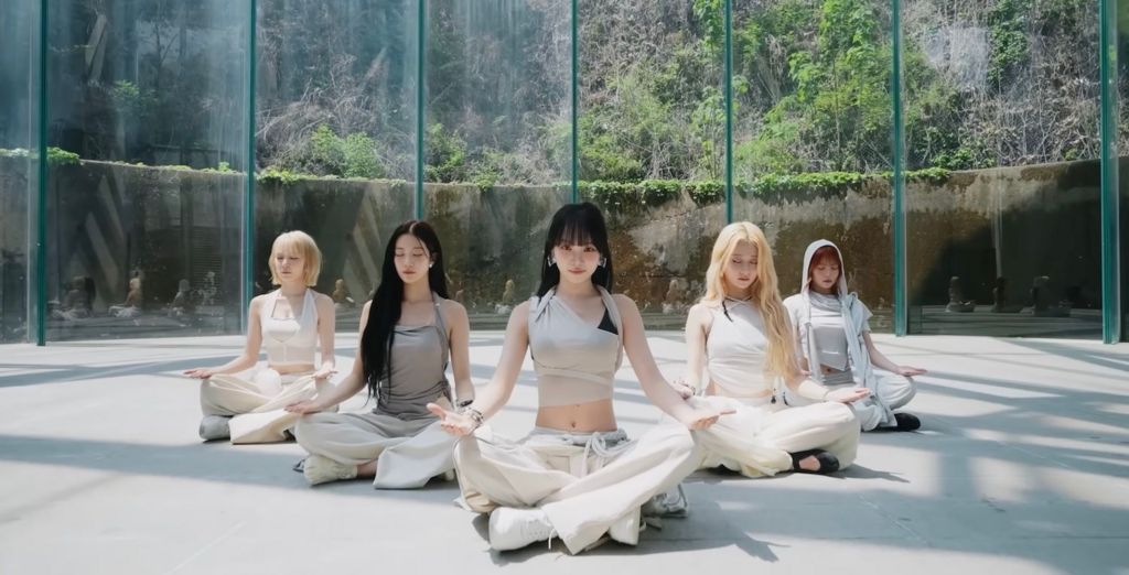 A still image from the performance video for Le Sserafim's song Boompala shows the band meditating in a plain room, whose windows look out onto a lush, mountainous backdrop