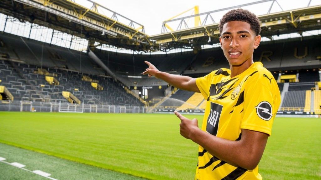 Jude Bellingham in a Borussia Dortmund shirt, stands on the edge of the pitch and points towards a stand in the distance behind him