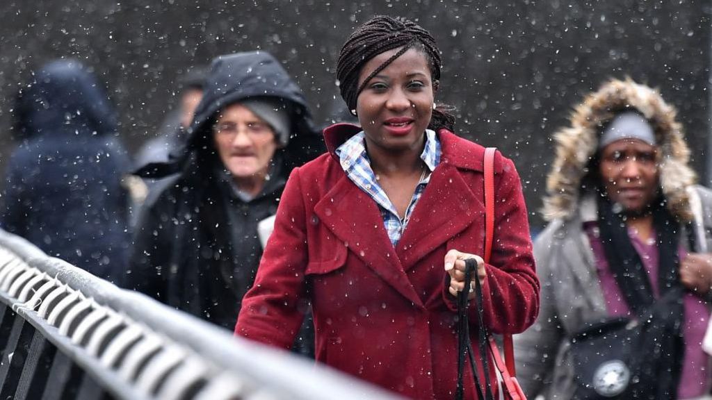 A woman wearing a bright red coat walks over a bridge with other commuters during a snow storm in Manchester. 