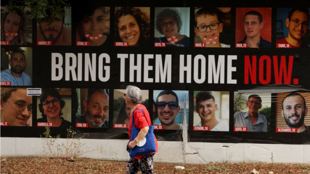 A woman walks past a poster with photos of hostages taken by Hamas  