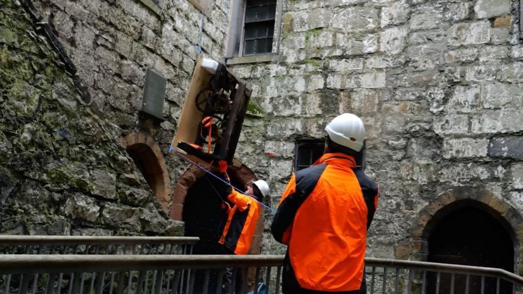 Workmen guiding the clock as it is lowered