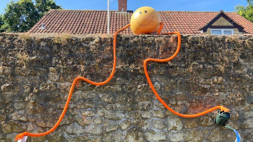 An orange ball with long dangly arms sitting on a wall