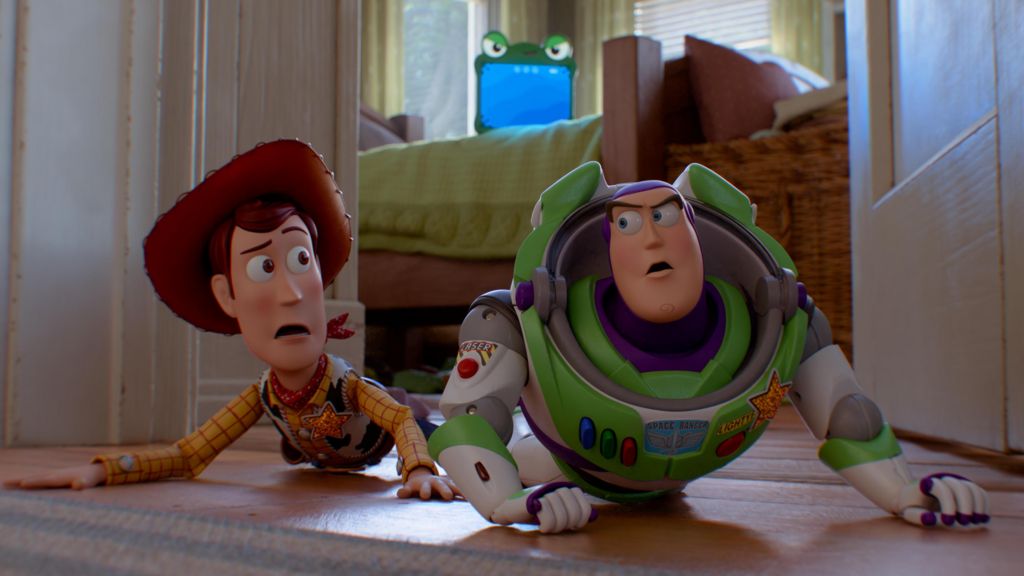 Woody and Buzz Lightyear in Toy Story 5, looking scared and crouching on the ground, with green tablet Lilypad seen in the background on the bed