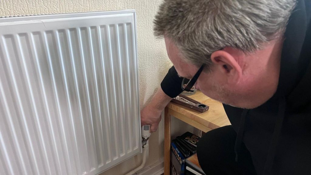 Man bending down adjusting the heating thermostat on an radiator