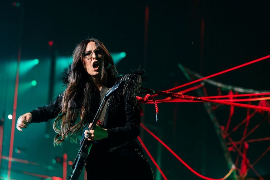 Veronica Fusaro plays guitar while straining against a web of red ropes