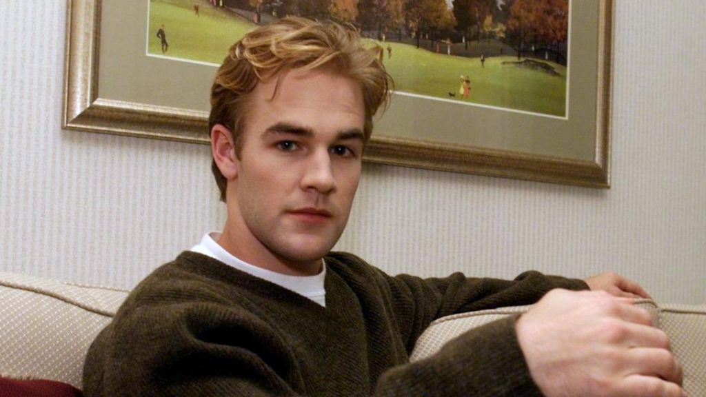James Van Der Beek wearing a brown jumper and white T-shirt, sitting on a sofa.