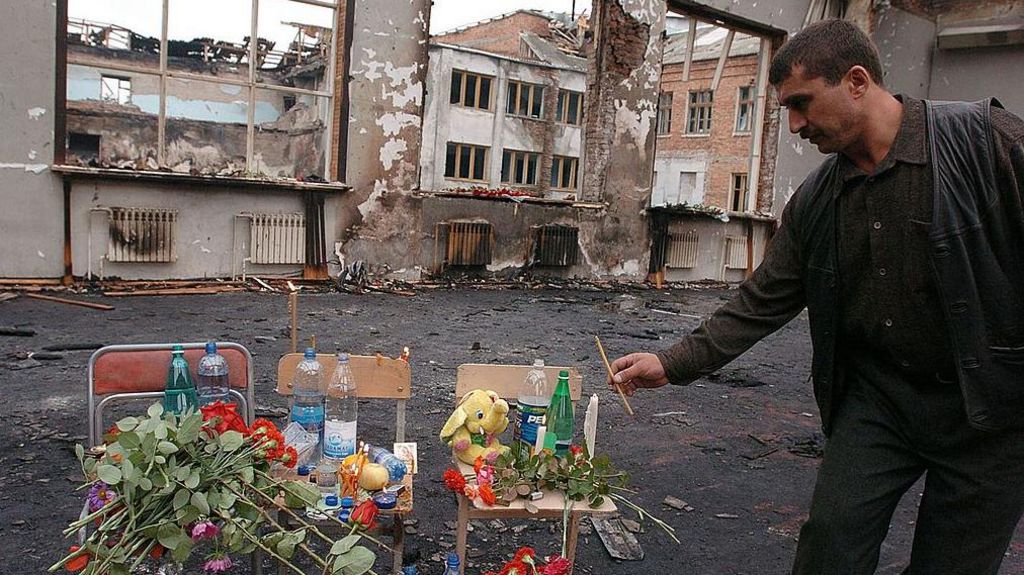 A man pays his respects at a makeshift memorial in the destroyed gym at the school