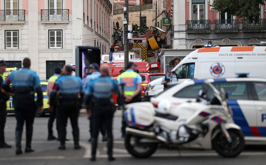 Police officers stand by near the scene of the crash with the overturned funicular seen crashed in the street above