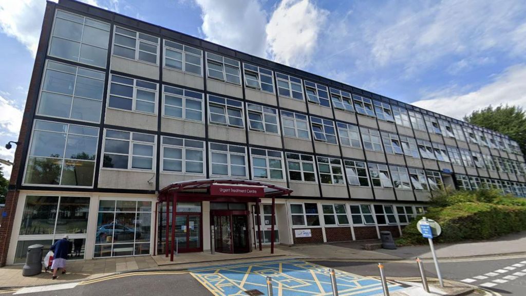 A Google Maps image of the exterior of Crawley Urgent Treatment Centre , an old hospital building with lots of windows and a burgundy coloured awning over a revolving door