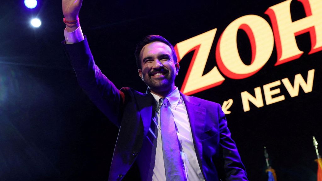 Zohran Mamdani holds his right arm up to wave after his victory speech