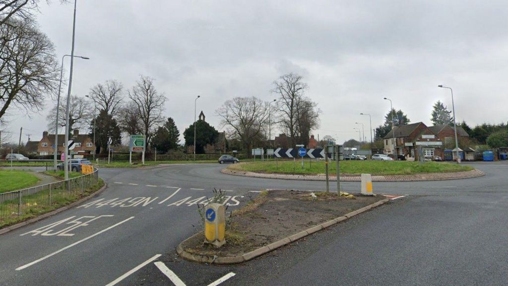 A roundabout with a footpath to the left hand side and bollards with directional arrows