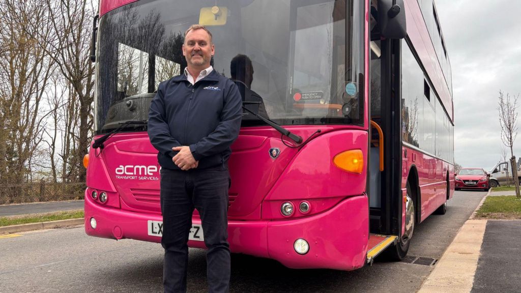 James Palmer stands in front of his parked bus. He is wearing his uniform, a zip-up top and dark trousers.