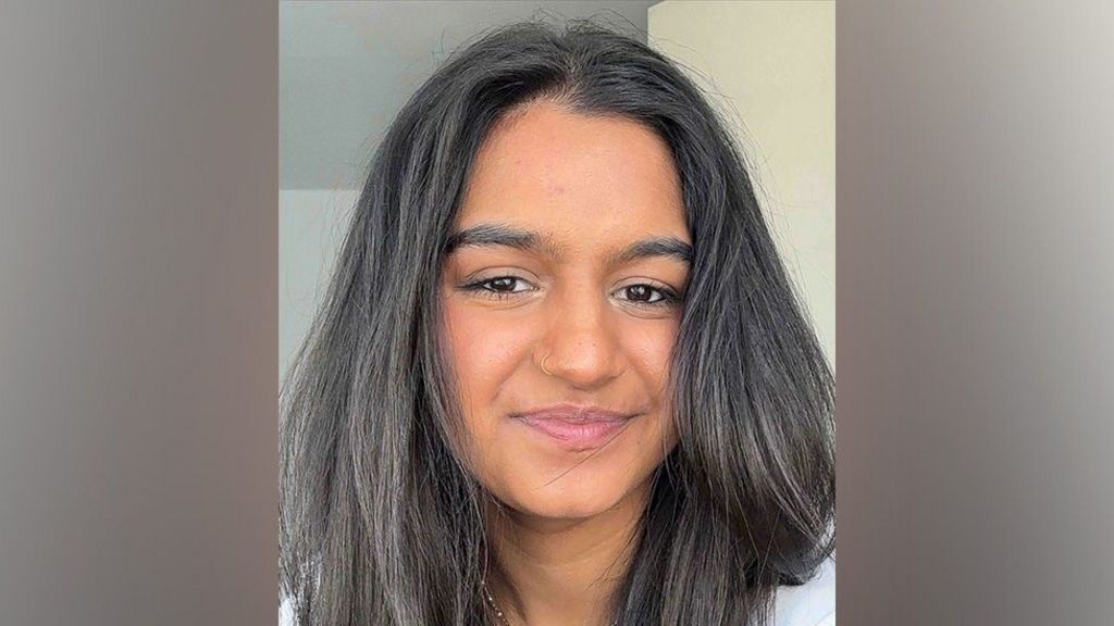 Aalia is smiling at the camera. She has long brown hair, brown eyes and a small nose ring