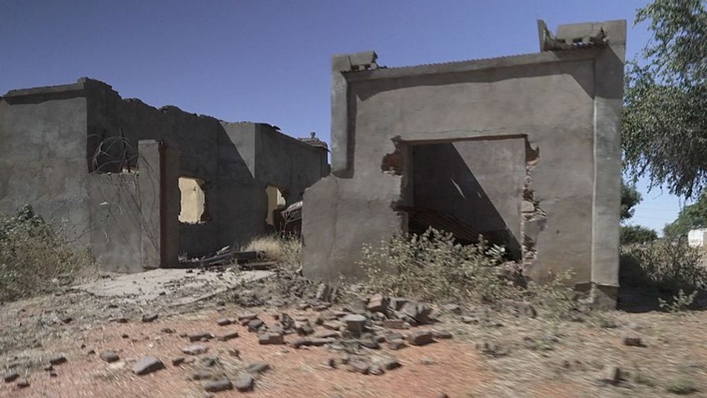 A grey, single-storey building appears damaged and deserted.