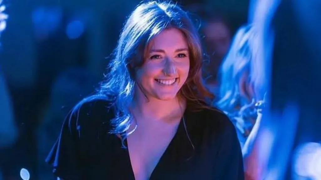 A smiling Jess Harper has shoulder-length dark hair and is wearing a black short-sleeved dress.