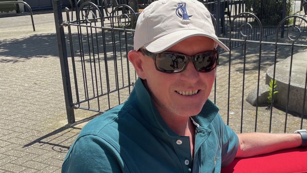 Richard Bendy is white and is wearing a blue/green T-shirt, with a white cap and sunglasses 