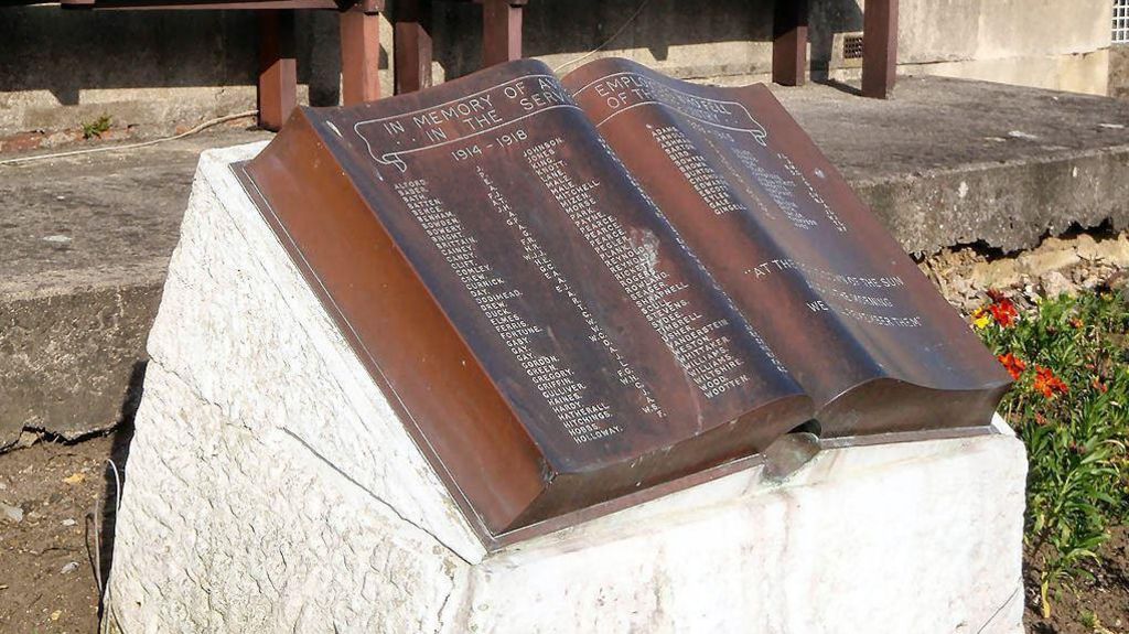 A copper book sitting on top of a white stone plinth. The book is engraved with about 100 names of soldiers who died in the world wars. 