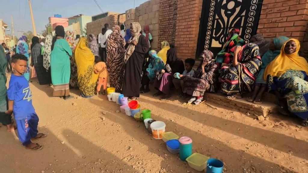 Residents wait to collect food in containers from a soup kitchen in Omdurman, Sudan