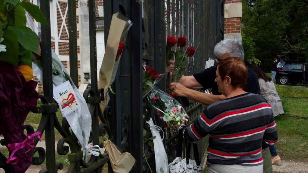 A couple attaches flowers on the gate of the entrance of the property of late French actor Alain Delon