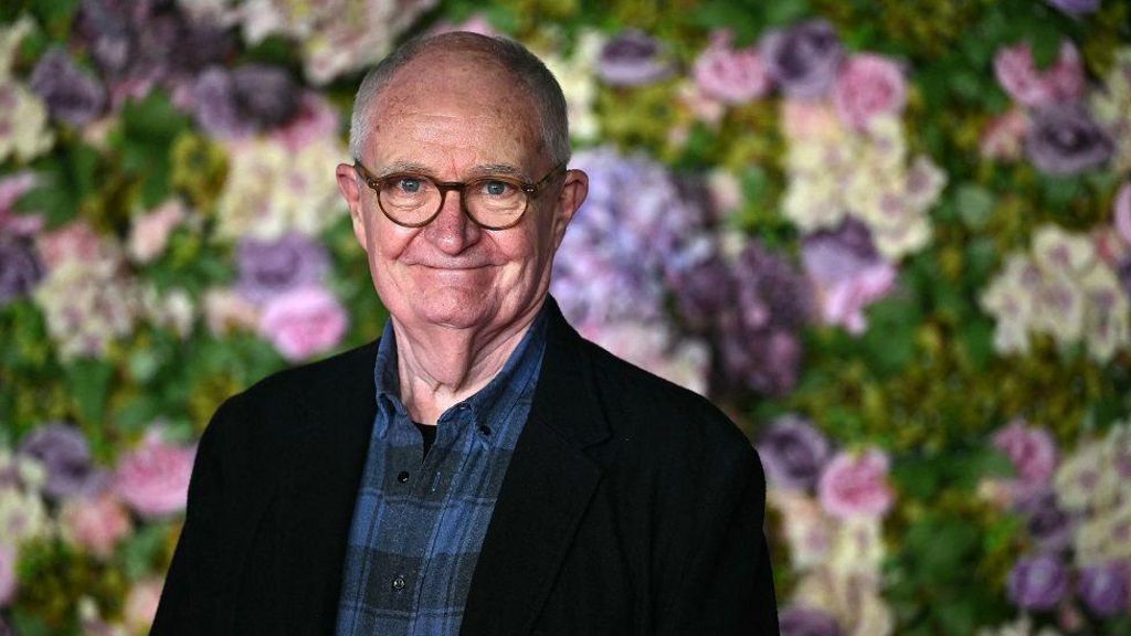 English actor Jim Broadbent smiles against a flower wall