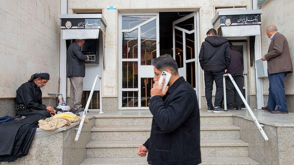 Men outside a bank using ATMs and one is walking by on his mobile phone.
