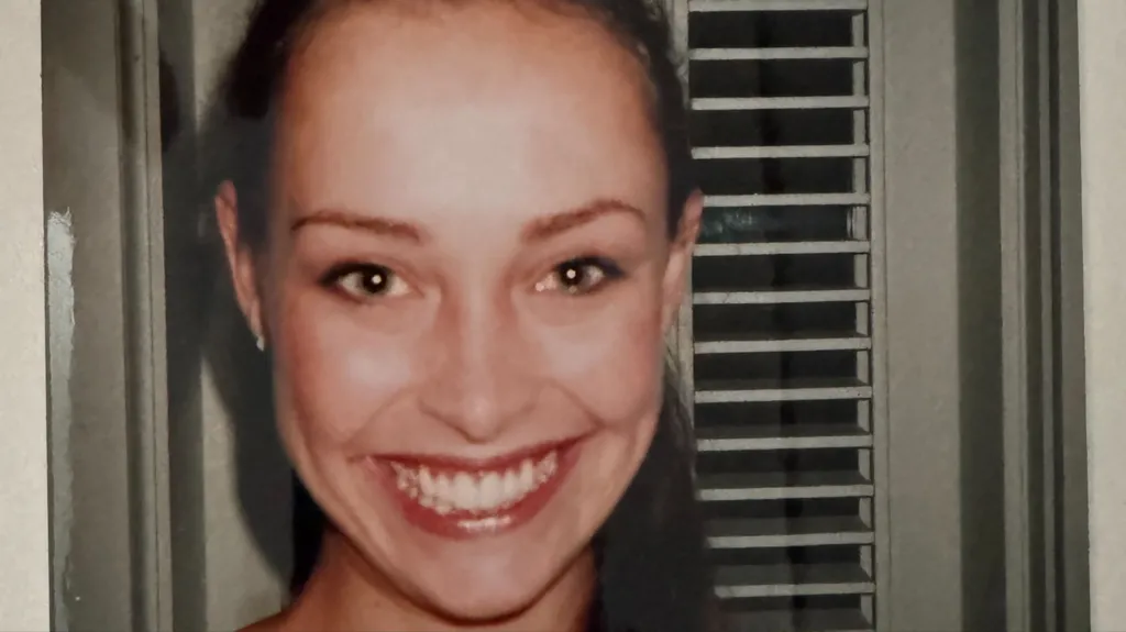 Juliette Bryant pictured in a headshot on Epstein's island in 2002. She is smiling and has her hair in a ponytail and is stood in front of a window with the blinds open at night 