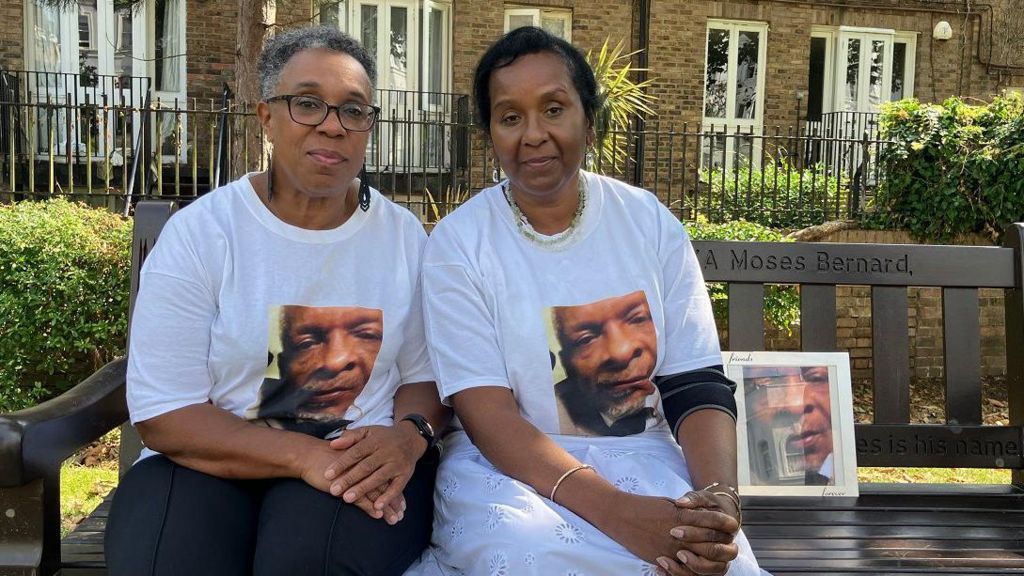 Jackie Leger (left) and Raymond's sister, Bernadette Bernard sit on a bench and look to camera. They are both wearing T shirts with Ray's face printed on them. 