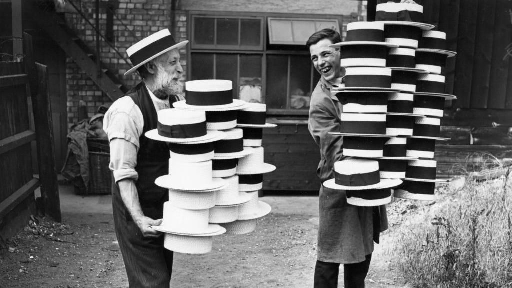 Hat manufacturers in Luton in 1928 carrying a pile of straw hats