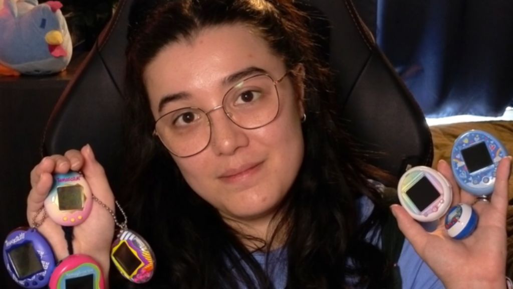 A young woman with dark brown hair and glasses holds multiple Tamagotchis in each hand