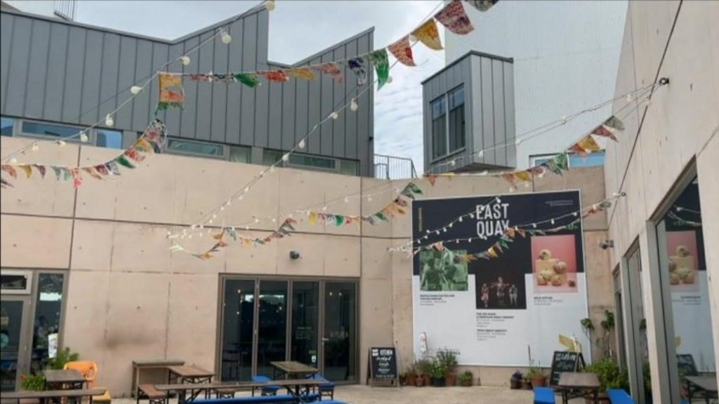 The outside of East Quay, showing a courtyard space with benches and lighting and bunting overhead. 