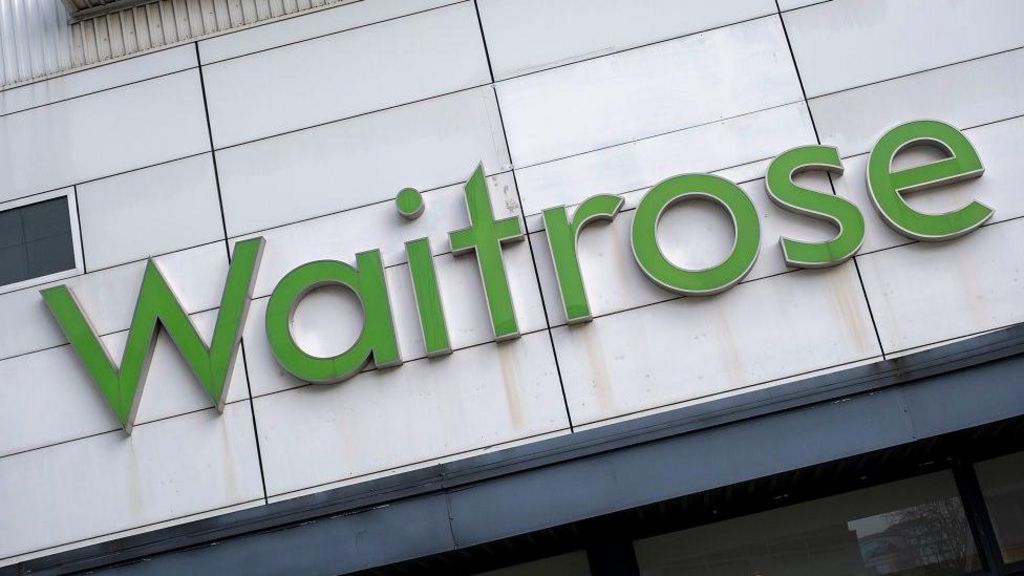 A sign above a door of a supermarket. It is in a light green font and reads: Waitrose